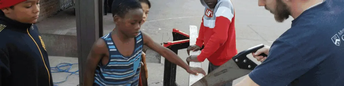 A student learning to use a hand saw with a volunteer